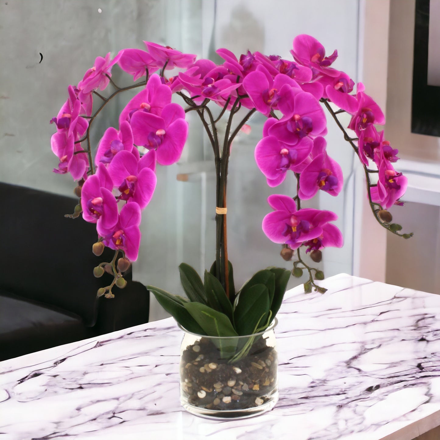 Real-touch delicate cascading orchids in a cylinder glass vase, with rocks and a water-like appearance. Recommended for indoor use.