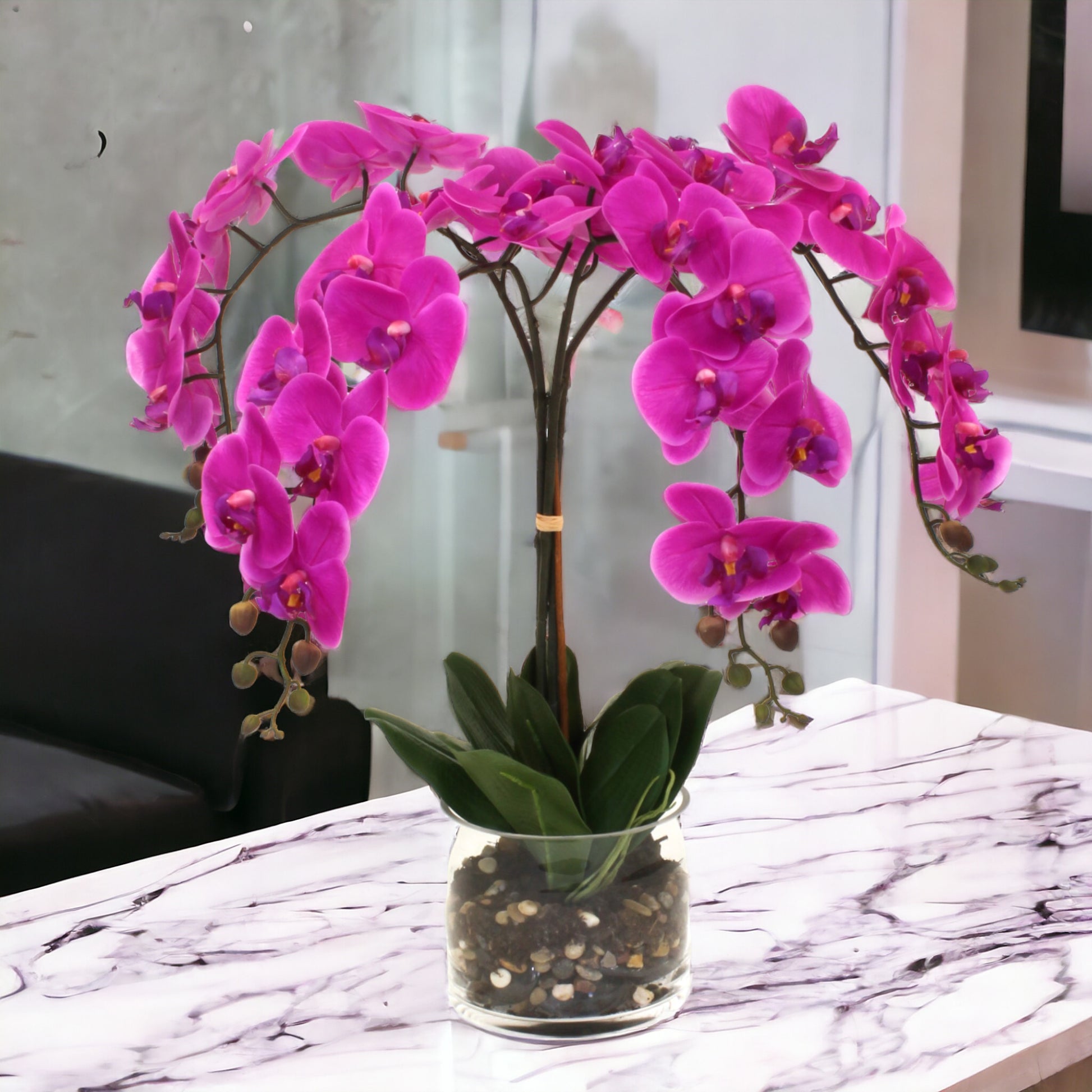 Real-touch delicate cascading orchids in a cylinder glass vase, with rocks and a water-like appearance. Recommended for indoor use.