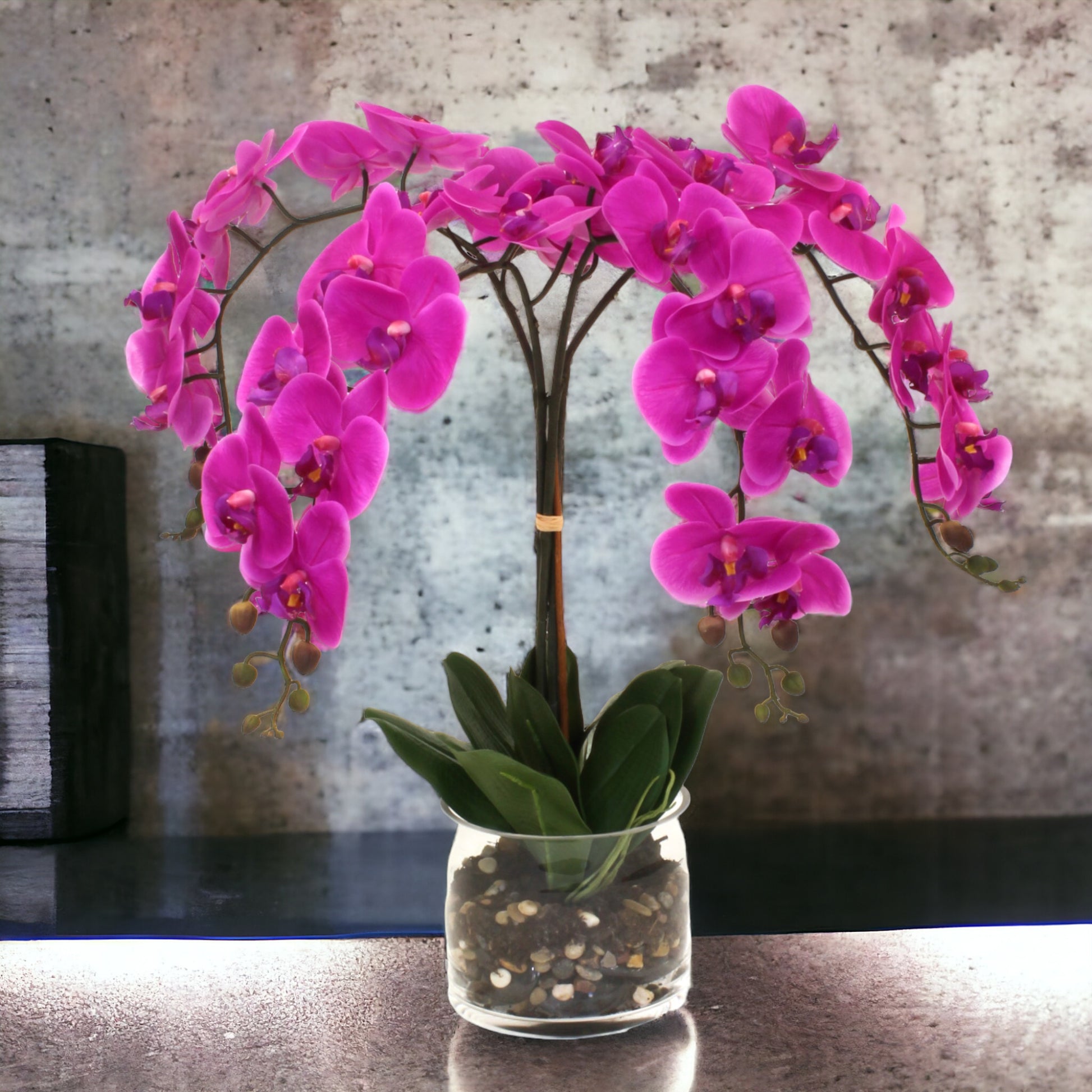Real-touch delicate cascading orchids in a cylinder glass vase, with rocks and a water-like appearance. Recommended for indoor use.