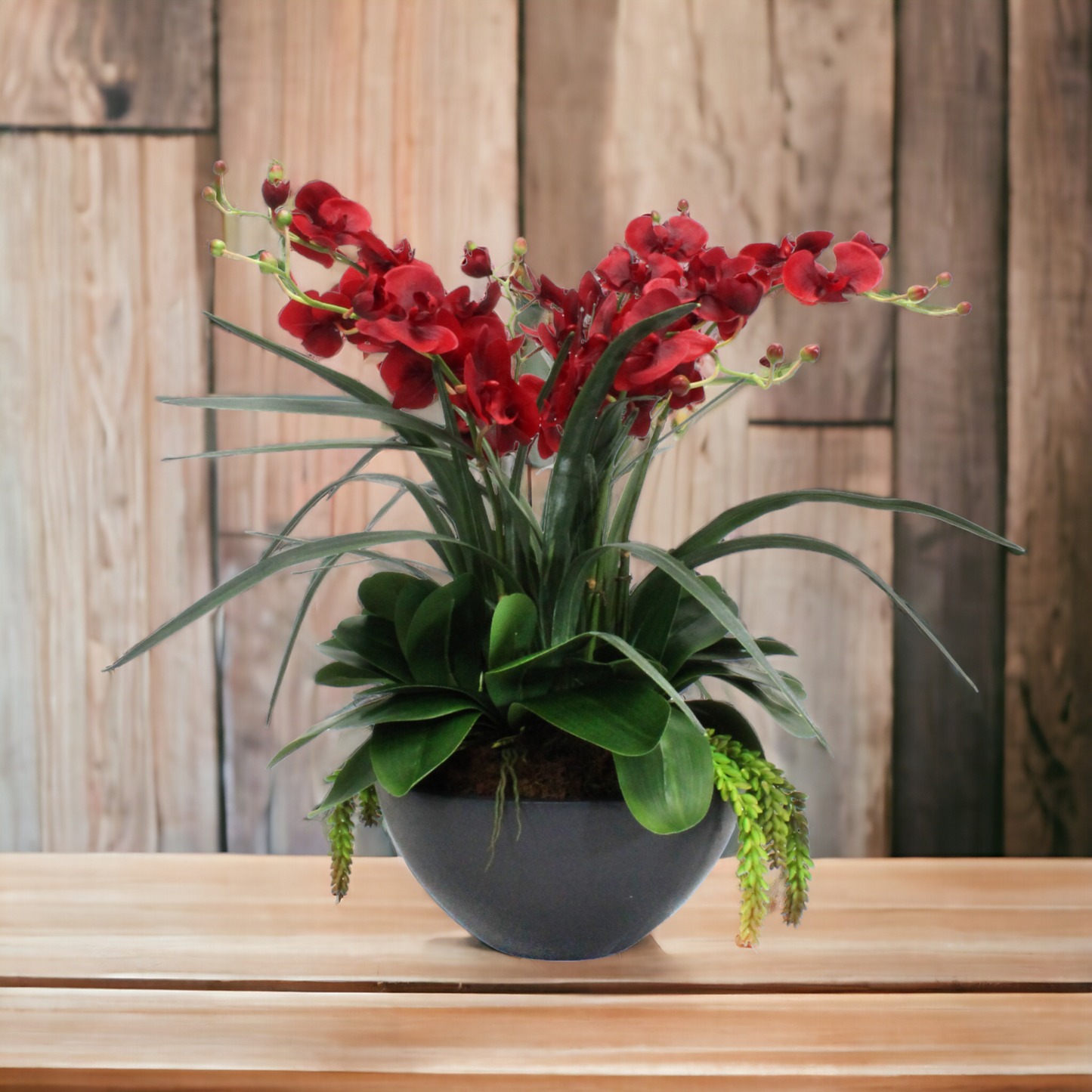 Real-touch delicate red orchids arranged in a heavy, dark ceramic bowl. The large-scale arrangement is designed to impress."
